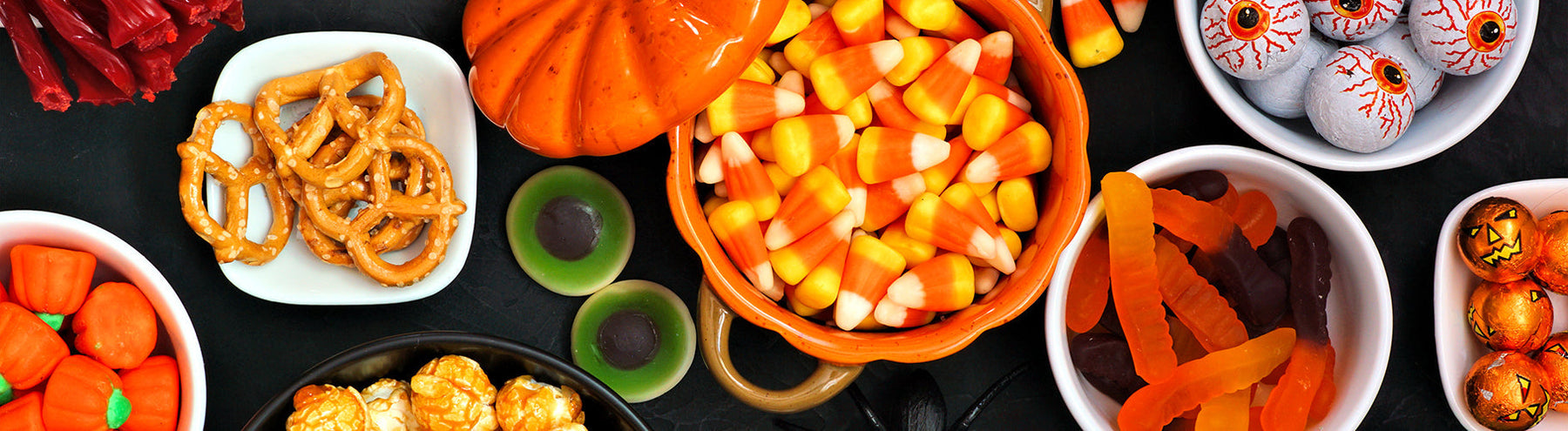 Fun Halloween-themed food table with candy corn, gummy worms, pretzels, candy eyeballs, licorice, and more.