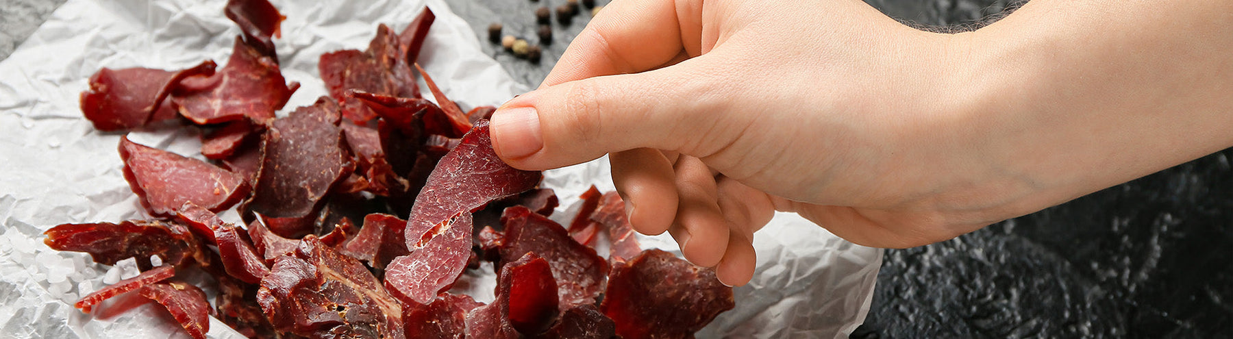 Hand reaching for high-protein beef jerky pieces.