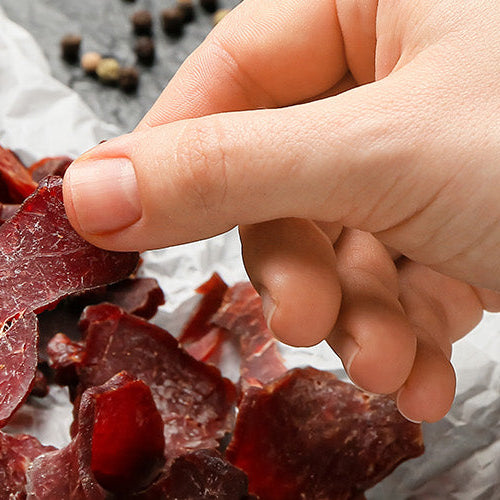 Hand reaching for high-protein beef jerky pieces.