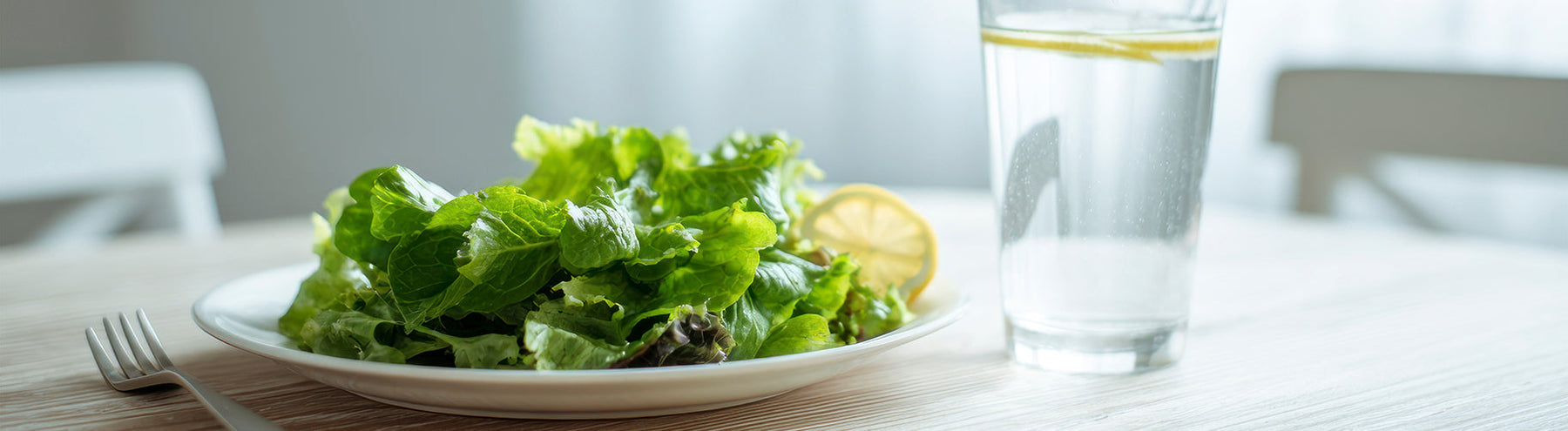 Fresh green salad with a glass of lemon water on a table, representing healthy eating and portion control.