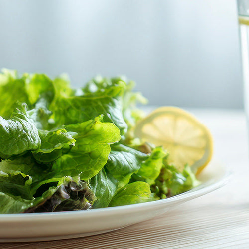 Fresh green salad with a glass of lemon water on a table, representing healthy eating and portion control.