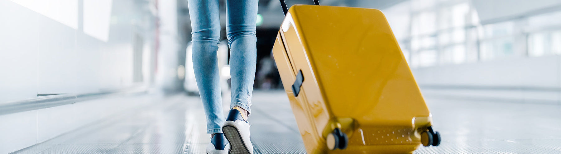 Traveler walking through an airport terminal pulling a yellow rolling suitcase.