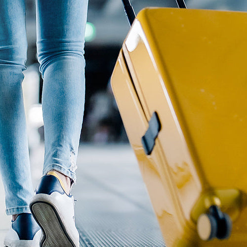 Traveler walking through an airport terminal pulling a yellow rolling suitcase.