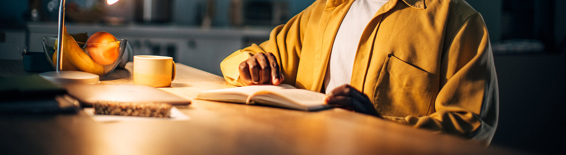 Person reading at their desk illuminated by a lamp.
