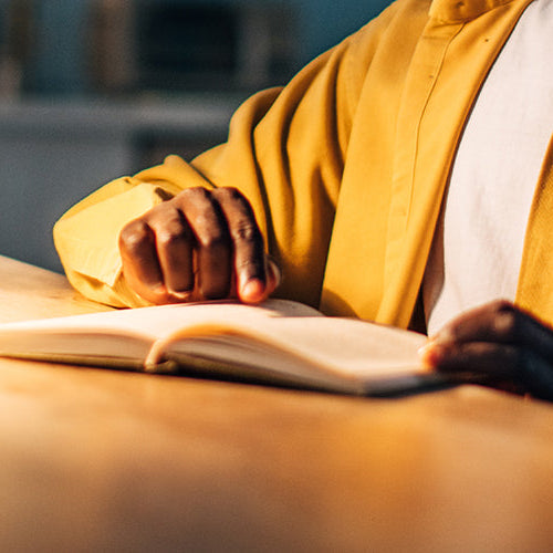 Person reading at their desk illuminated by a lamp.
