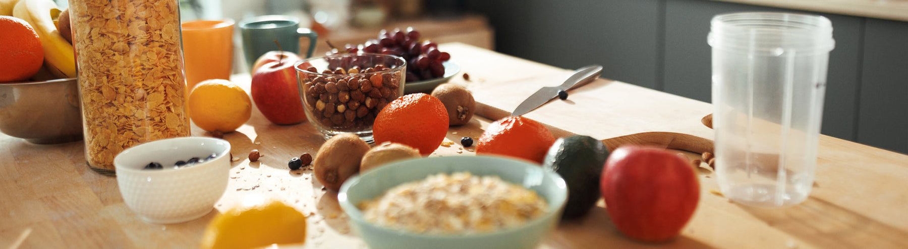 Healthy breakfast ingredients including oats, fruit, nuts, and a shaker cup arranged on a kitchen countertop.