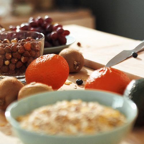 Healthy breakfast ingredients including oats, fruit, nuts, and a shaker cup arranged on a kitchen countertop.