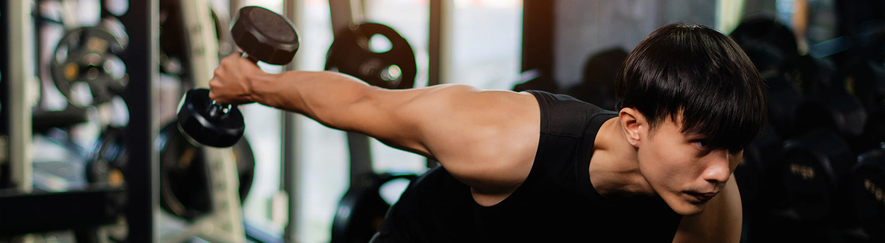 Man performing a dumbbell tricep kickback exercise in a gym during a strength training workout.