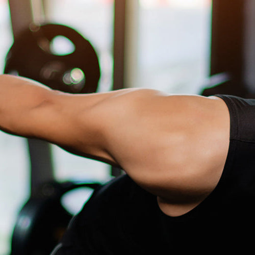 Man performing a dumbbell tricep kickback exercise in a gym during a strength training workout.