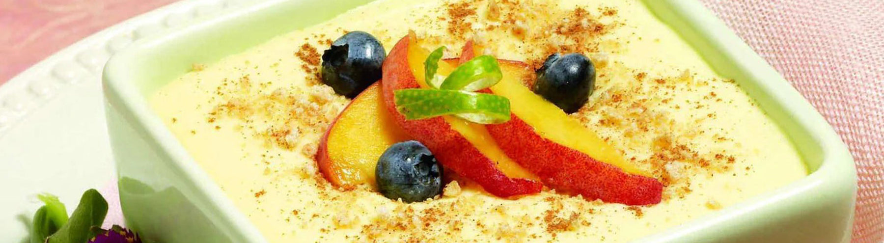 Creamy dessert topped with sliced peaches, blueberries, and a light dusting of cinnamon in a square dish.