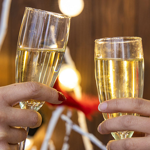 Two people toast a glass of champagne in front of holiday lights.