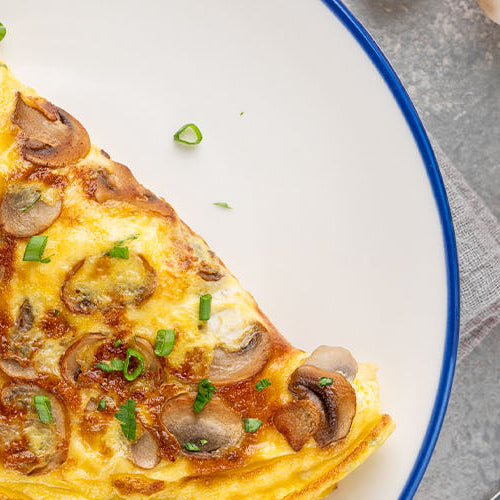Mushroom omelette garnished with herbs on a white plate, with fresh tomatoes and greens nearby.