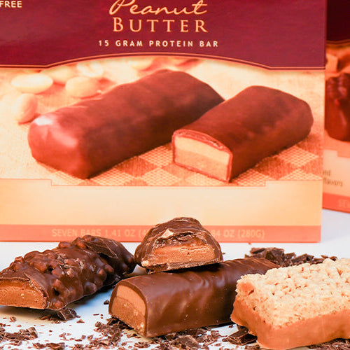 Assorted Nutmeg State Nutrition high protein bars displayed in front of their packaging, featuring flavors like Crunch, Peanut Butter, and Gourmet Nut.