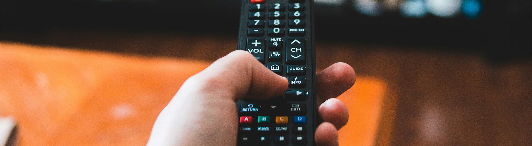 Close-up of a person holding a remote control towards the TV and clicking the enter button.