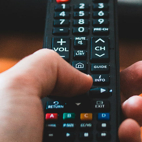 Close-up of a person holding a remote control towards the TV and clicking the enter button.