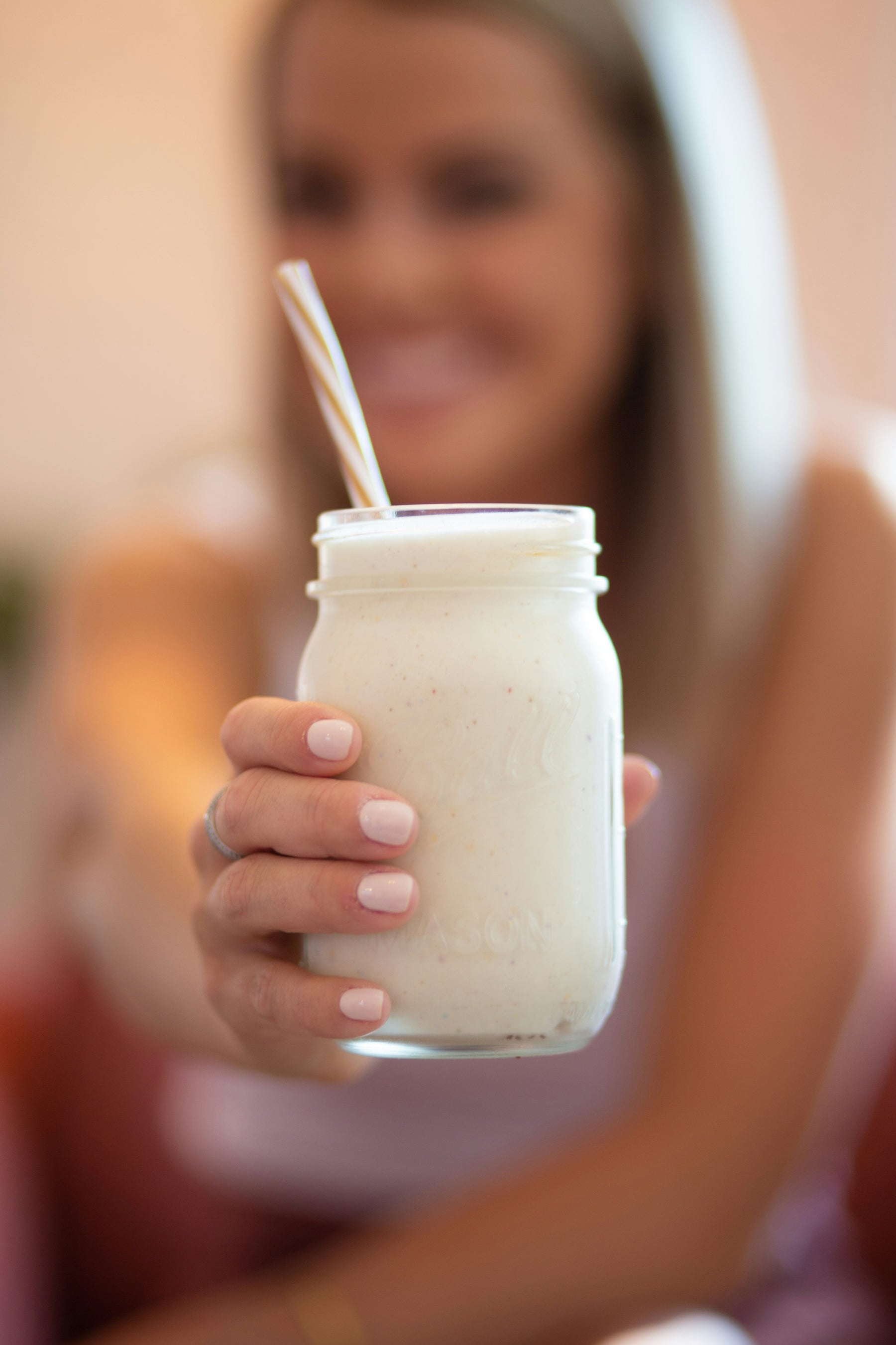 Young woman holding out a vanilla protein shake in front of her.