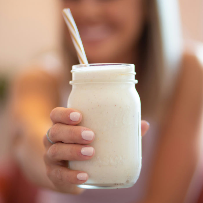 Young woman holding out a vanilla protein shake in front of her.